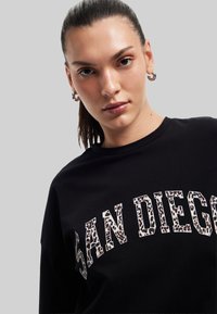 Mustapohjainen puuvillapaitasweater, jossa on eläinkuosilla painettu "SAN DIEGO", pyöreä kaula-aukko ja rento malli. Sileä pinta, pitkät hihat.