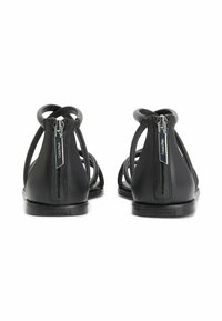 Sandales en cuir noir avec un design à brides, dotées d'une fermeture éclair arrière et d'une semelle plate. Matière en cuir de veau et accents minimalistes en métal.