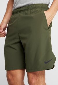 Pantalones cortos deportivos de color verde oscuro con una cinturilla elástica, bolsillos laterales y un logotipo negro de Nike en el lado inferior izquierdo. Textura de tela suave.