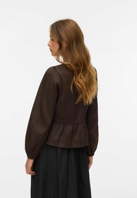 Smeđi, teksturirani bluzon s napuhanim rukavima i peplum rubom. Nosiv s crnom suknjom koja ima glatki, leteći dizajn.