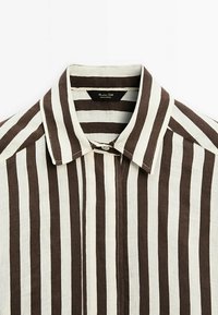 Chemise à col avec des rayures verticales marron et blanches, boutonnée en haut, l'étiquette indique "Massimo Dutti Fabriqué au Portugal."