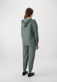 Green cotton hoodie with a hood, relaxed fit, paired with matching tapered pants. Smooth texture and elasticized cuffs and waistband.