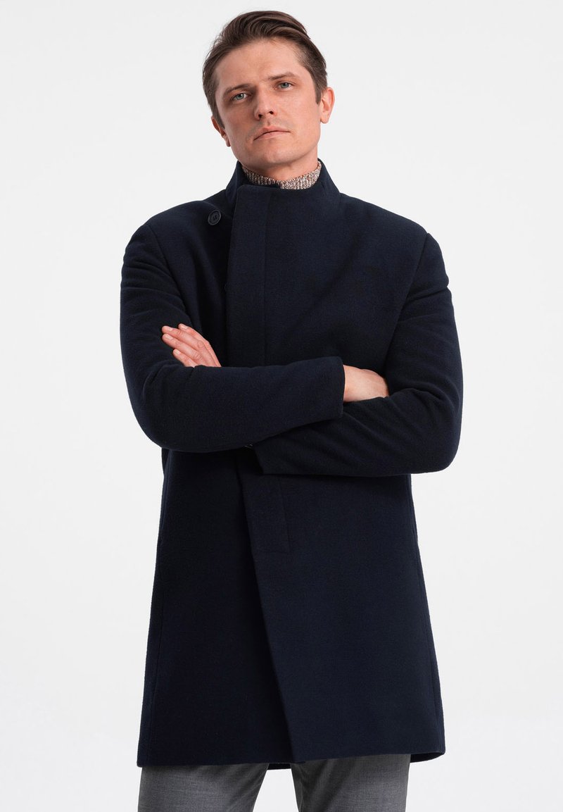 Laine navy long manteau avec un col haut, fermeture à un bouton et poches latérales. Texture lisse, coupe ajustée et design minimaliste.