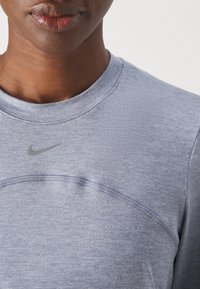 Šedá mikina Nike s kulatým výstřihem. Vyznačuje se jemnou texturou a kontrastním šitím. Logo na hrudi je zobrazeno ve stříbrné barvě.