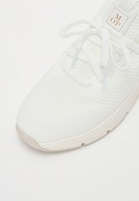 Sneaker de sport blanche avec une tige en mesh texturé et respirant, des lacets plats et une semelle légèrement rembourrée. Logo affiché sur la languette.