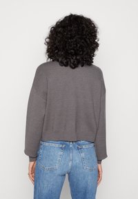 Pull en gris raccourci avec des épaules tombantes, des poignets et un ourlet côtelés, associé à un jean en denim bleu taille haute, avec des poches arrière.