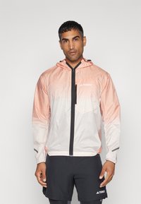 Lett, hettejakke i en gradient av rosa og hvit. Har frontglidelås, brystlomme og elastiske mansjetter. Laget av pustende stoff.