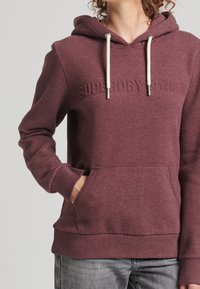 Bordeauxkleurige hoodie met een kangoeroezak, trekkoordsluiting en reliëflogo op de voorkant. Gemaakt van een zachte stoffenmix.