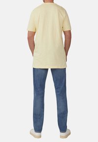 Korte mouwen heren shirt in het geel met een ronde halslijn, gecombineerd met blauwe jeans en witte sneakers, gezien van achteren.