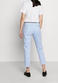 Blaue und weiße gestreifte Hosen mit schmaler Passform, ausgestattet mit zwei Gesäßtaschen und einem schmalen Bund. Kombiniert mit einem schlichten weißen T-Shirt.