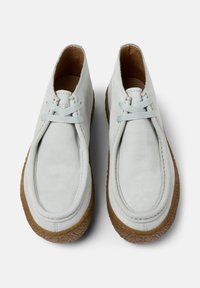 Zapatos de cuero gris claro con puntas redondeadas y cordones finos, con una suela marrón texturizada, mostrados desde una perspectiva cenital.
