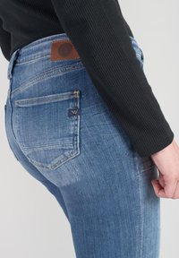 Skinny blue jeans made of denim with a mid-rise waist, subtle whiskering, and a leather patch on the back waist. Minimalistic design.