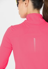 Enges pinkes Sportoberteil mit hohem Kragen, strukturiertem Stoff und reflektierenden Streifen auf dem Rücken für bessere Sichtbarkeit.