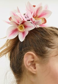 Fermaglio per capelli a forma di orchidea rosa con petali dettagliati e un centro giallo, posizionato su capelli castano chiaro, caratterizzato da un design di chiusura robusto.