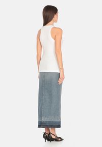 Top bianco senza maniche abbinato a una lunga gonna di jeans con un lavaggio blu sbiadito e orlo blu scuro. Tacchi neri con cinturini completano l'outfit.