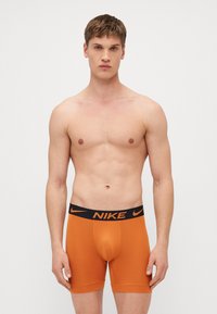 Boxers laranja com uma faixa elástica preta com o logótipo da Nike, textura suave, design ajustado e corte de comprimento médio.