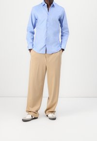 Vaaleansininen napitettava paita, khakinväriset leveälahkeiset housut ja harmaalla koristellut kengät. Paidassa on kaulus ja pitkät hihat; rento istuvuus.