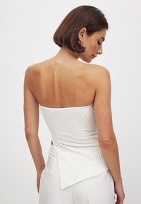 Witte strapless top van textuurstof, met een lichte asymmetrische zoom en een aansluitend ontwerp. Gladde, ribbelige oppervlakte zonder patronen.