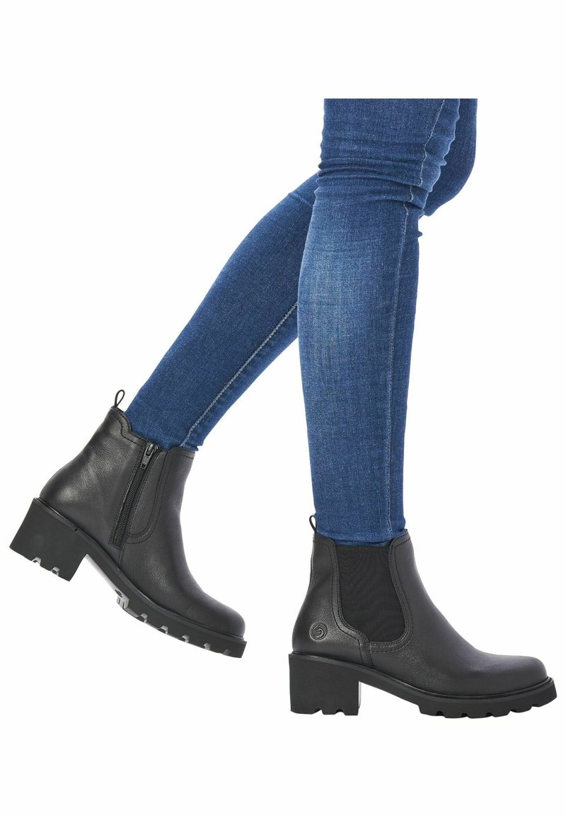 Black leather ankle boots with elastic side panels, textured surface, and block heels. Worn with blue denim skinny jeans.