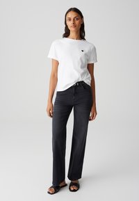 Witte katoenen t-shirt met opgerolde mouwen, gecombineerd met hoge, donkere jeans en zwarte schuifsandalen. Eenvoudig ontwerp met minimale details.
