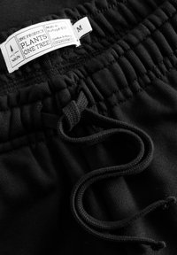 Schwarze Sportshorts mit elastischem Bund und verstellbarem Kordelzug. Features ein Pflegeetikett und den Text: "Ein Produkt pflanzt einen Baum."