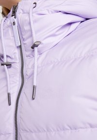 Veste matelassée violet clair avec fermeture éclair, cordons blancs avec embouts métalliques et capuche.