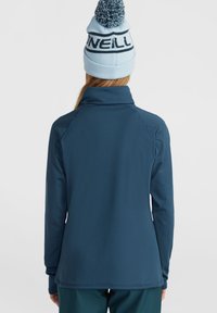 Pullover lungo blu navy con collo alto, realizzato in tessuto liscio e elastico. Caratterizzato da una silhouette aderente e polsini con foro per il pollice.