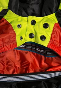 Tissu jaune et rouge avec des boutons-pression noirs et une bande élastique rayée, montrant l’étiquette intérieure du vêtement avec le texte « killtec ».