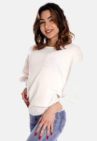 Maglione bianco in maglia con una vestibilità rilassata e maniche ampie, abbinato a jeans blu. Texture liscia e design minimalista.