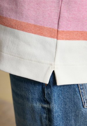 Zbliżenie na podszyty dzianinowy t-shirt w różowe, pomarańczowe i białe paski na tle niebieskich dżinsów.