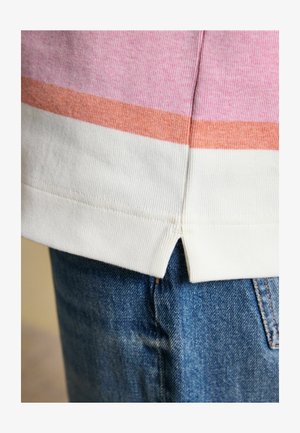 Zbliżenie na podszyty dzianinowy t-shirt w różowe, pomarańczowe i białe paski na tle niebieskich dżinsów.