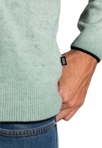 Miętowy sweter o prążkowanej strukturze z czarnymi akcentami przy mankietach i dolnym brzegu. Posiada małą czarną metkę z napisem "DRD" z boku.