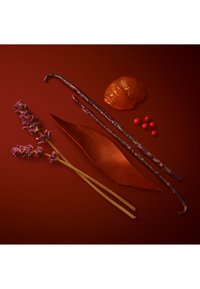 Due bacche di vaniglia, una foglia marrone, un pezzo di resina ambra traslucida, sei piccole perle rosse e due rametti di lavanda viola su uno sfondo rosso scuro.