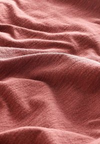 Texturovaná tkanina v jemné, tlumené růžové barvě, vykazující jemné vlnění a sklady, s subtilními variacemi tónu a hladkým povrchem.