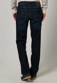 Mörkblå denimjeans med rak passform, har en läderpatch på midjan och dekorativa sömmar på bakfickorna.