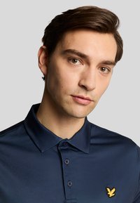 Marine polo-shirt gemaakt van gladde stof, met een klassieke kraag, knoopsluiting en een klein geel adelaarslogo op de borst.