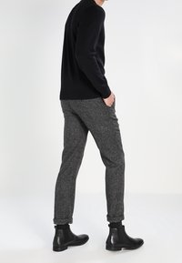 Svart tröja, grå texturerade byxor och svarta ankelstövlar. Slim fit, uppvikta fållar på byxorna, elegant design utan synliga mönster.