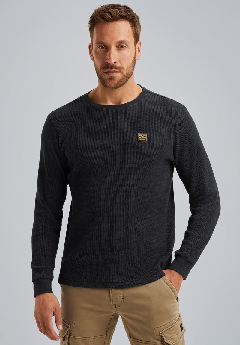 Dunkelgraues Langarmshirt aus strukturiertem Stoff, mit rundem Ausschnitt und einem kleinen gelben Logo-Patch auf der Brust.