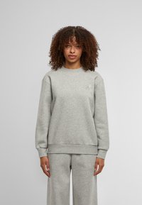 Pilkas džemperis su apvalia iškirpte, raštuotomis rankovėmis ir apačia. Subtilus logotipo detalė kairėje krūtinės pusėje. Tekstūruota medžiaga su minkštu paviršiumi.