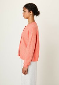 Koralen pleteni jopič s sproščenim krojem, okroglo izrezom in dolgimi rokavi. Mehka tekstura in zapiranje s kratkimi gumbi.