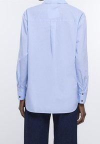 Ljusblå långärmad skjorta med uppvikt krage, ryggryn och knappade manschetter. Slät tyg med en något strukturerad passform.