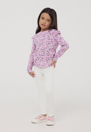 Camicia a maniche lunghe di colore rosa chiaro con dettagli a volant e motivi colorati di caramelle e unicorni, abbinata a leggings bianchi e scarpe slip-on pastello.