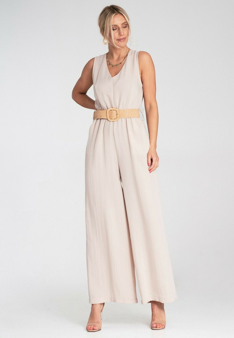 Beżowy, bezrękawnikowy kombinezon wykonany z miękkiego materiału, z dekoltem w serek i szerokim pasem ściągniętym słomkowym paskiem. Gładka tekstura z szerokimi, zwiewnymi nogawkami.