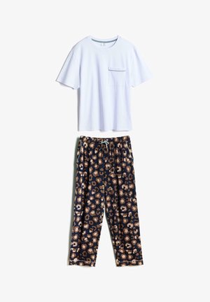 Männlicher Torso hebt weißes Hemd, zeigt braune Haut, trägt dunkle Shorts mit braunem und beigem Tiermuster und eine hellblaue Kordel.
