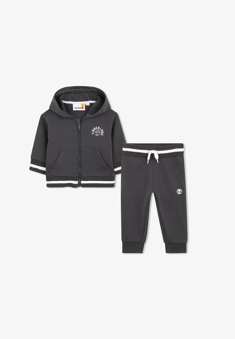 Sweat à capuche gris foncé pour tout-petit avec fermeture éclair et pantalon assorti, ornés de bandes blanches et des logos Timberland sur la poitrine et la jambe.