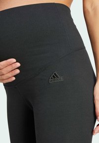 Leggings de maternidad negros con relieve, de cintura alta, con un pequeño logo negro de Adidas en el costado y una textura suave y elástica.
