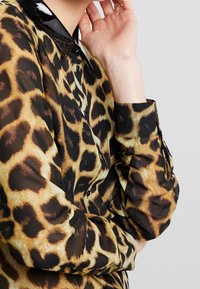 Leopard print blouse with black glossy collar, long sleeves, and buttoned cuffs, featuring a sheer texture and bold, contrasting patterns.