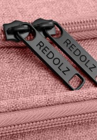 Roze stoffen ritszak met een textuurovervlak. Twee zwarte ritslifts met het label "REDOLZ" bevestigd aan een bijpassende rits.
