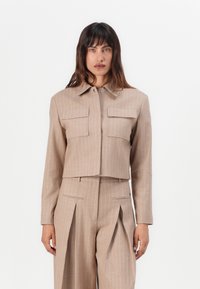 Beige cropped jakke med vertikale striper, to frontlommer og spiss krage, kombinert med matchende høy midje plissert bukser.