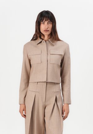 Beige cropped jacket with vertical pinstripes, two front pockets, and a pointed collar, paired with matching high-waisted pleated trousers.
